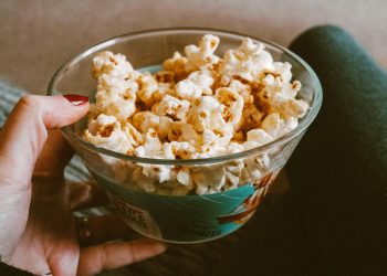 Close-up of a hand holding a glass bowl filled with delicious popcorn. Perfect snack time capture.