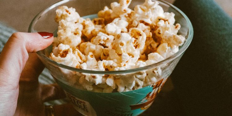 Close-up of a hand holding a glass bowl filled with delicious popcorn. Perfect snack time capture.