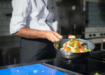 Professional chef tossing fresh vegetables in a frying pan in a modern kitchen.