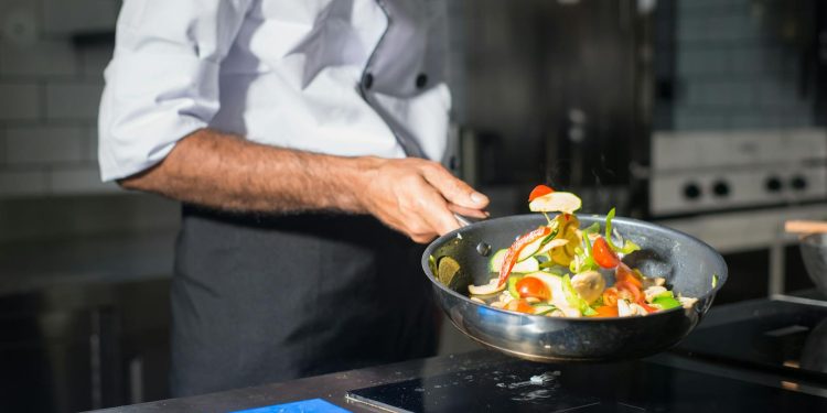 Professional chef tossing fresh vegetables in a frying pan in a modern kitchen.