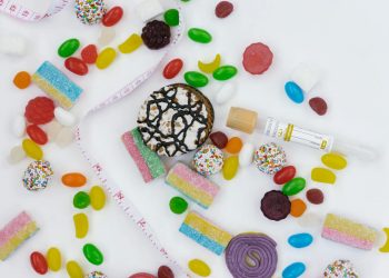 Top view of assorted candies, cookies, and a tape measure symbolizing unhealthy diet choices.