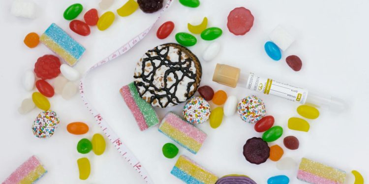 Top view of assorted candies, cookies, and a tape measure symbolizing unhealthy diet choices.